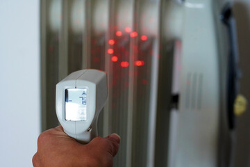 hand with a non-contact digital infrared thermometer measuring the temperature and correct operation of a white radiator