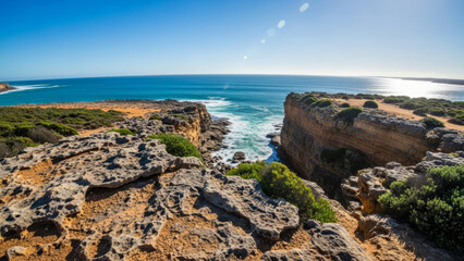 Stunning Australian wild coastal landscape with rocky cliffs and ocean waves. Beautiful scenery on rugged terrain with clear blue skies and vibrant greenery. Ideal for travel blogs,