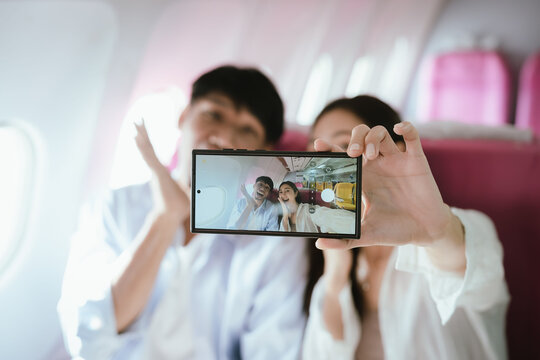 Young Asian couple taking a selfie on an airplane while holding passports, capturing a happy travel moment and representing modern tourism, mobility, and vacation lifestyle.