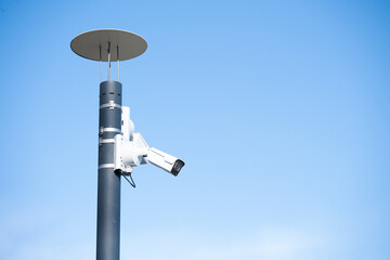 Modern CCTV surveillance camera mounted on a metal pole against a clear blue sky. Outdoor security system with copy space, minimalistic composition and clean background.