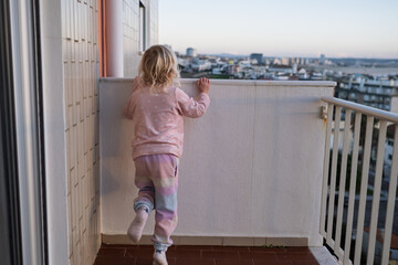 Little Girl Standing on Balcony Looking at City, Danger of Leaving Child Alone