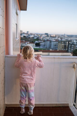 Little Girl Standing on Balcony Looking at City, Danger of Leaving Child Alone