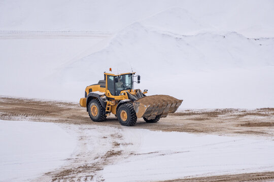 Wheel loader transporting sand in winter quarry, heavy construction machinery operating on snowy excavation site during cold weather