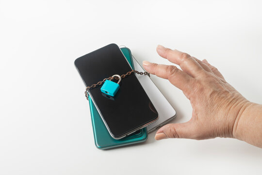 A hand reaches for a stack of cell phones, chained and locked. Information overload, digital fatigue, digital detox. Digital addiction