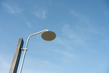 Outdoor public shower head mounted on a metal pole against a clear blue sky. Minimalistic composition with copy space, symbolizing hygiene, refreshment, summer