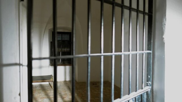 An empty old prison cell, taken from outside while door is open. the cell door is closing and back opens, while the shadows are casting on the floor and walls. a 4K video clip.