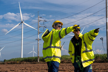 Workers discuss project details at wind farm site during bright day with turbines in background