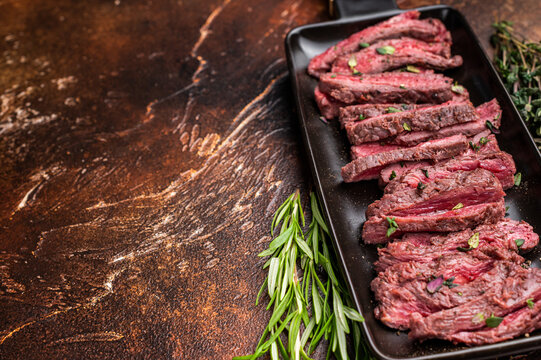 BBQ Grilled Flank beef steak, sliced meat with herbs, brown background. top view