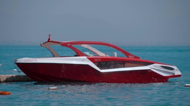 A beautiful red motorboat rocks on the sea waves, and the sun's rays and wave crests are reflected off its sides. Slow mo, slow motion, high speed camera