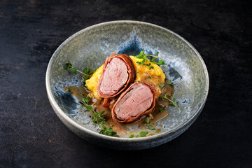 Pork fillet roast wrapped in prosciutto ham bacon with polenta and fresh herbs served as close-up...
