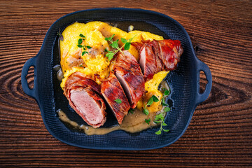 Pork fillet roast wrapped in prosciutto ham bacon with polenta and fresh herbs in serving cast iron skillet