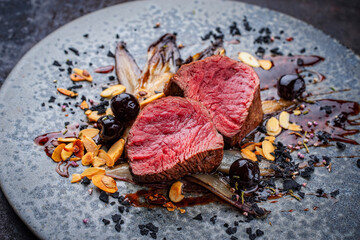 Fine dry aged beef filet steak rare tataki style cut tagliata with caramelized chicor&eacute;e, amarena cherry and almonds served as close-up on a design plate