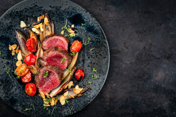 Fine dry aged beef filet steak rare tataki style cut tagliata with caramelized chicor&eacute;e, tomato and almonds served as top view