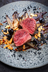 Fine dining dry aged beef filet steak rare tataki style cut tagliata with caramelized chicor&eacute;e, amarena cherry and almonds served as top view on a design plate