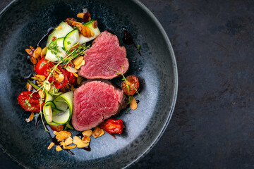 Fine dry aged beef filet steak rare tataki style cut tagliata with sliced zucchini, tomato and almonds served as top view on a design plate