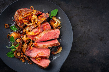 Zwiebelrostbraten roast beef - sirloin beef steak braised with fried onion rings and mushrooms served as top view on a design plate with copy space right