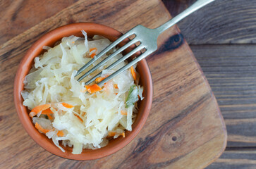 A ceramic brown bowl with homemade sauerkraut and carrots on a burlap napkin in a rustic style