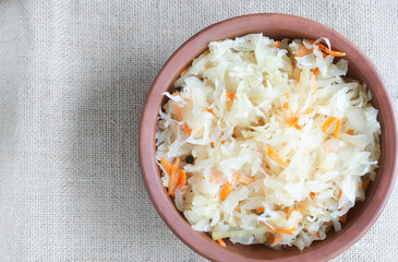 A ceramic brown bowl with homemade sauerkraut and carrots on a burlap napkin in a rustic style