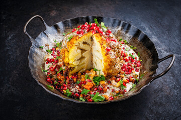 Vegetarian dish - whole oven baked roasted cauliflower with tahini sauce, chickpeas and pomegranate in rustic iron skillet pan