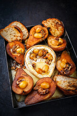 Oven baked camembert cheese with caramelized glazed pears, walnuts and grapes and baguette served as close-up on rustic metal sheet