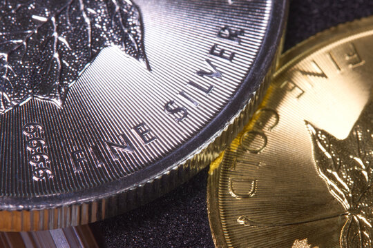 Close-up of the inscription &ldquo;fine silver&rdquo; on a silver coin lying on a gold coin labeled &ldquo;fine gold,&rdquo; representing precious metal prices and the gold-to-silver ratio.