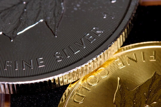 Close-up of the inscription &ldquo;fine silver&rdquo; on a silver coin lying on a gold coin labeled &ldquo;fine gold,&rdquo; representing precious metal prices and the gold-to-silver ratio.