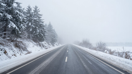 Fototapeta premium Empty snow covered highway stretching into the distance during a foggy winter day