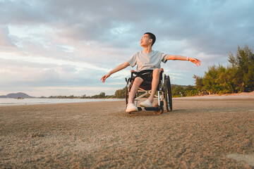 Young Asian man using wheelchair enjoying freedom at the beach during sunset, arms open with peaceful expression. Inclusive travel, disability lifestyle, and emotional outdoor moment.