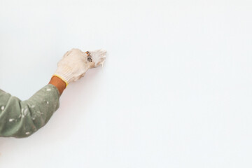 Gloved hand applying white paint to a smooth wall in white background.