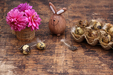 Quail eggs with flowers and Easter bunnies on a shabby wooden board with text space.
