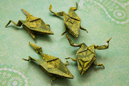 Flat lay view of four cute origami frogs in patterned paper set on green paper background - Powered by Adobe