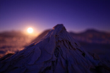 Dramatic mountain peak illuminated by a glowing sun during a hazy twilight scene with purple skies and atmospheric mist