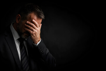 Depressed businessman covering face in despair against black background with copy space