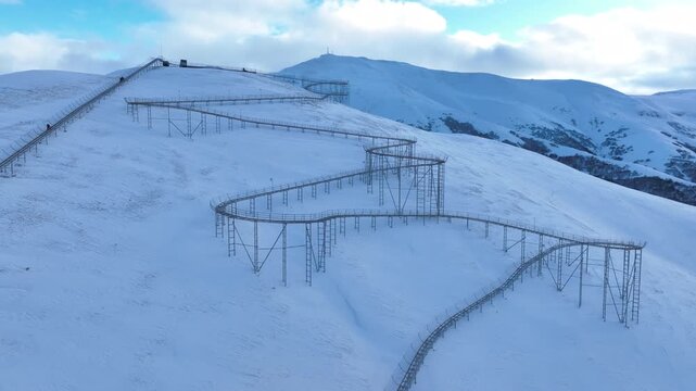 Drone view of a bobsled mountain coaster winding through the snow-covered Caucasus mountains in Bakuriani resort, featuring people enjoying the winter attraction.