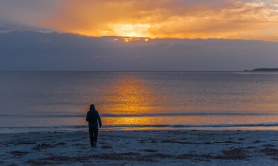 Fototapeta premium Silhouette of a man walking alone on the beach at sunset