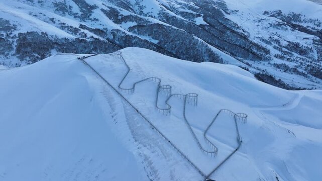 Drone view of a bobsled mountain coaster winding through the snow-covered Caucasus mountains in Bakuriani resort, featuring people enjoying the winter attraction.