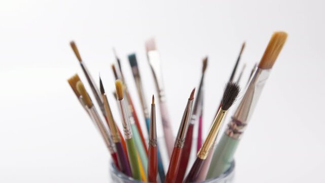 Art brushes for painting in a glass jar rotating on a white background.