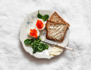 Delicious breakfast, brunch, tapas, snack - boiled eggs with red caviar, toasts with butter, spinach on a light background, top view