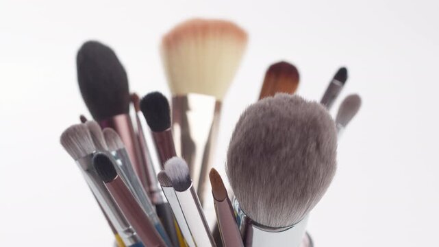 Female hand choosing a professional makeup brush from a diverse set. Close-up of beauty tools collection isolated on white background.