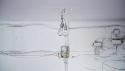 Temporary lighting in a building renovation. Dirty electric bulbs hanging from the ceiling with chaotic painted cables and sloppy wiring on the blurred background. Photo