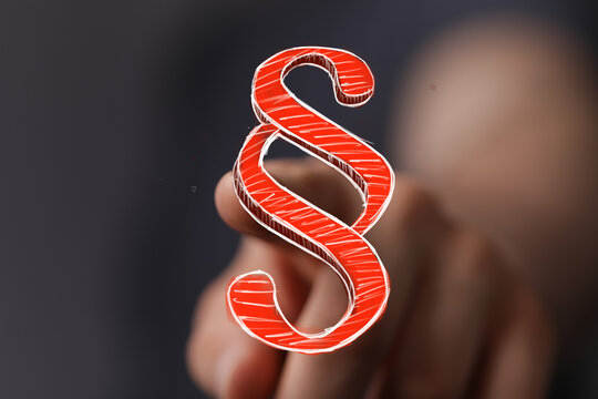 A glowing red paragraph symbol digitally displayed with a human hand pointing, representing legal advice, justice, and regulations. Ideal for la