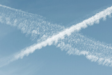 Traînées de condensation d'avions formant un « X » dans un ciel bleu clair