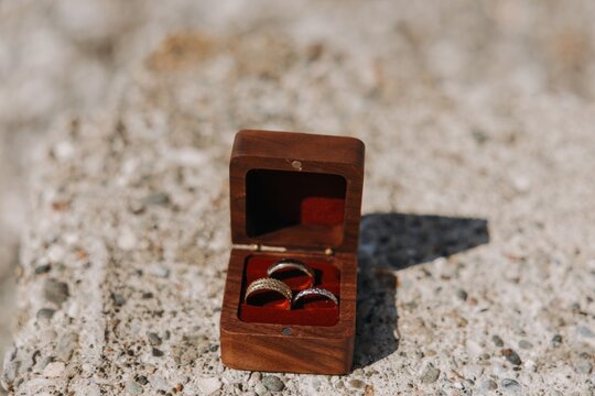 Three wedding rings with different textures placed in a luxury wooden box with red velvet lining on a stone surface outdoors