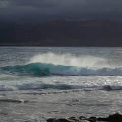 Gran Canaria, view towards Atlantic ocean from El Confital beach on the edge of Las Palmas de Gran Canaria, big waves crushing, rain in the mountains
