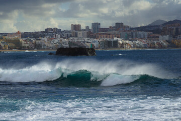 Gran Canaria, view towards Atlantic ocean from El Confital beach on the edge of Las Palmas de Gran Canaria, big waves crushing, rain in the mountains
