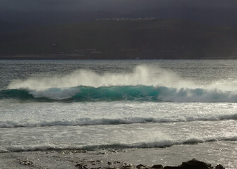 Gran Canaria, view towards Atlantic ocean from El Confital beach on the edge of Las Palmas de Gran Canaria, big waves crushing, rain in the mountains
