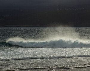 Gran Canaria, view towards Atlantic ocean from El Confital beach on the edge of Las Palmas de Gran Canaria, big waves crushing, rain in the mountains
