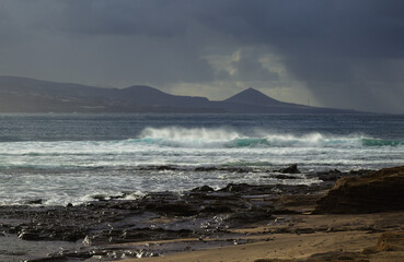 Gran Canaria, view towards Atlantic ocean from El Confital beach on the edge of Las Palmas de Gran Canaria, big waves crushing, rain in the mountains
