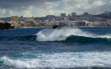 Gran Canaria, view towards Atlantic ocean from El Confital beach on the edge of Las Palmas de Gran Canaria, big waves crushing, rain in the mountains
