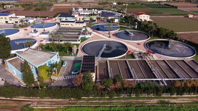 Aerial view of a modern wastewater treatment plant in Spain as the camera slides left, revealing circular clarifiers, filtration basins, solar panels, and organized water processing infrastructure
